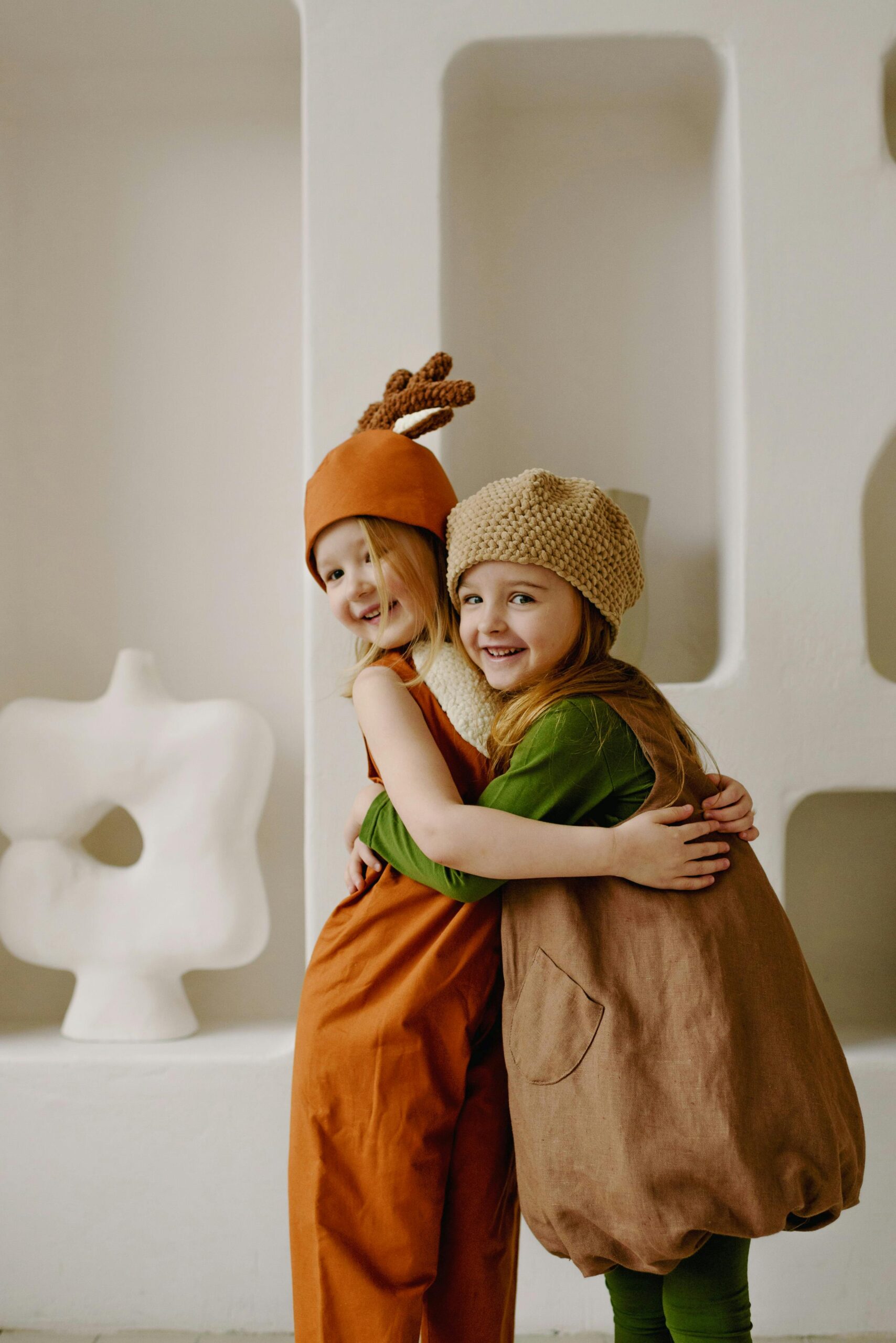 Two children in playful costumes embrace indoors, highlighting joy and friendship.